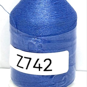 May include: A spool of blue thread with a green top and a white base. The label on the spool reads "Z742". The thread is tightly wound, and the spool is cylindrical.