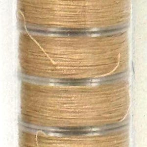 May include: A clear plastic tube containing several spools of tan thread. The label on the tube reads "Z647" in bold black font. The thread appears to be tightly wound and ready for use.