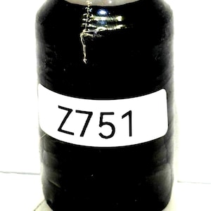 May include: A spool of black thread with a white label displaying the number "Z751". The thread is tightly wound on a cylindrical core. The top of the spool is a light gold color with text. Ideal for sewing and crafting projects.