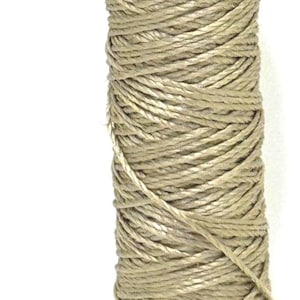 May include: A spool of beige-colored thread, tightly wound and textured. The label reads "SOIE PURE" and "603 PURE T004". The thread is likely used for sewing, embroidery, or other textile crafts.