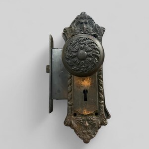 May include: Antique brass door knob and lock set with ornate detailing. The knob has a floral design and the lock plate has a keyhole.