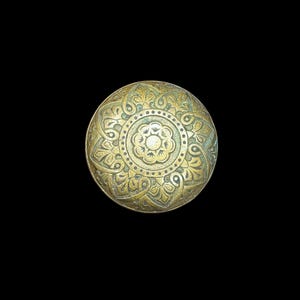 May include: A round, antique brass knob with an intricate floral design. The knob features a central flower surrounded by detailed patterns and a slightly aged patina. The background is solid black.
