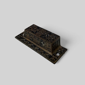 May include: A vintage, ornate, bronze-colored door pull with intricate geometric designs. The pull is rectangular with a raised center section and a decorative border.