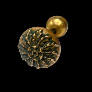 May include: A gold door knob with a detailed floral design. The knob is round and has a raised design of leaves and a flower in the center.