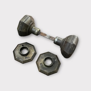 May include: A set of antique door knobs with octagonal escutcheons. The knobs are made of brass and have a worn, aged finish.