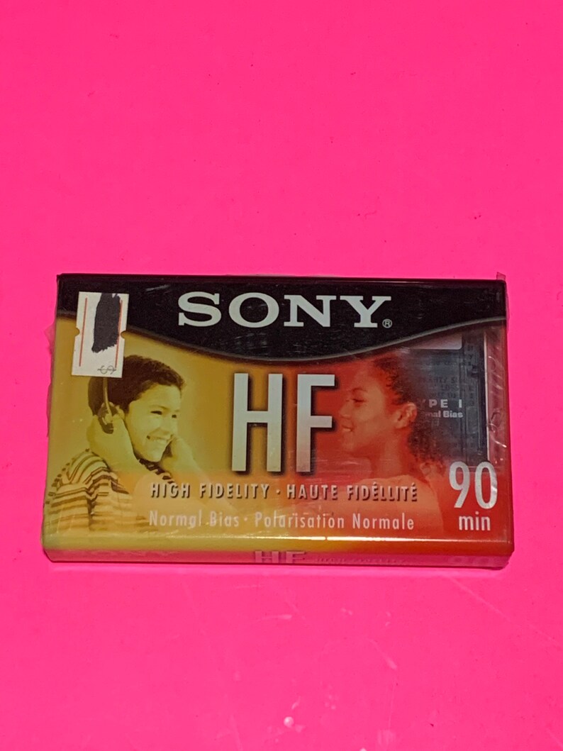 May include: A vintage Sony HF 90 min audio cassette tape. The cassette features the Sony logo and the text "HF HIGH FIDELITY". The packaging shows images of people listening to music. The cassette is on a pink background.