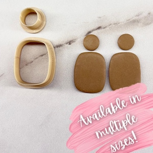 Puede incluir: Un conjunto de cortadores de arcilla polimérica beige y dos pendientes de arcilla marrón. Los cortadores incluyen un círculo, un rectángulo y dos pendientes con la parte superior redondeada y una base rectangular. Texto en una pincelada rosa: "¡Disponible en múltiples tamaños!"