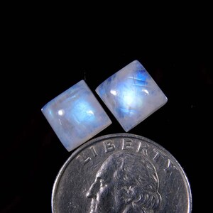 May include: Two square-shaped moonstone cabochons with a blue iridescent sheen, next to a US quarter for size comparison.
