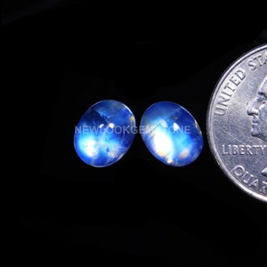 May include: Two oval-shaped blue moonstone cabochons, each approximately the size of a US quarter.