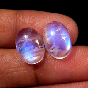 May include: Two oval-shaped moonstone cabochons with iridescent blue and white colors.