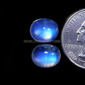 May include: Two oval-shaped moonstone cabochons, one blue and one white, with a blue sheen. The stones are approximately the size of a US quarter.