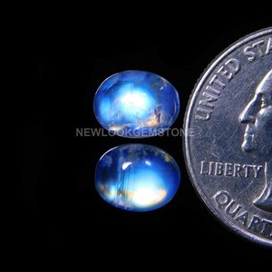 May include: Two oval-shaped moonstone cabochons, one blue and one light blue, with a rainbow sheen. The stones are about the size of a US quarter.