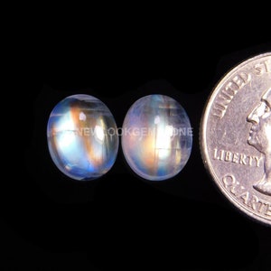 May include: Two round, iridescent moonstone cabochons, approximately 1/2 inch in diameter, with a rainbow of colors, including blue, green, and gold. The stones are next to a US quarter for size comparison.