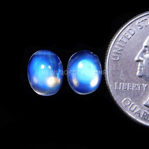 May include: Two oval-shaped blue moonstone cabochons, each approximately the size of a US quarter.
