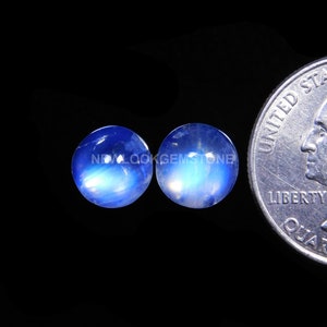 May include: Two round, blue moonstone cabochons, each approximately 1/2 inch in diameter, are displayed next to a US quarter for size comparison.