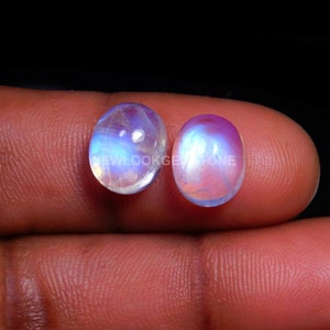May include: Two oval-shaped moonstone cabochons with iridescent blue and white colors. The stones are approximately 1 inch in length.