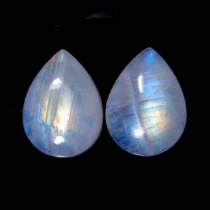 May include: Two teardrop-shaped moonstone cabochons with iridescent blue and white colors.