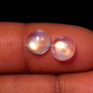 May include: Two round, iridescent moonstone cabochons with a rainbow sheen. The stones are approximately 10mm in diameter and have a smooth, polished surface.