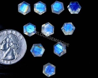 May include: A collection of hexagonal moonstone gemstones with a blue and white iridescent glow. A US quarter is included for size reference. The gemstones are displayed on a black background.