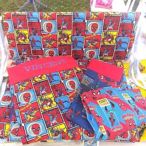 Op de afbeelding: Een set van rode, blauwe en gele stof met een Spiderman-patroon. De stof is in verschillende vormen en maten geknipt. De stof heeft de woorden "Spider-Man" en "Marvel Comics" erop gedrukt. De stof heeft ook de naam "Vincent" geborduurd.