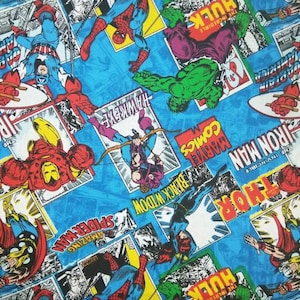 Può includere: Un tessuto blu con un motivo ripetuto di copertine di fumetti con supereroi Marvel, tra cui Iron Man, Thor, Hulk, Black Widow e Spider-Man. Il testo sulle copertine include "The Incredible Hulk", "Thor", "The Invincible Iron Man", "Marvel Comics", "Amazing Spider-Man", "Black Widow" e "Hawkeye".