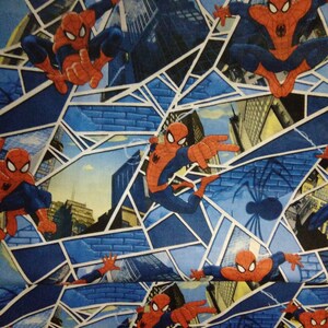 May include: A blue and white fabric with a repeating pattern of Spiderman in a red and blue suit, swinging from a web in front of a cityscape. The background is a blue and white web pattern.