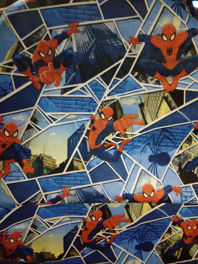 May include: A blue and white fabric with a repeating pattern of Spiderman in a red and blue suit, swinging from a web in front of a cityscape. The background is a blue and white web pattern.
