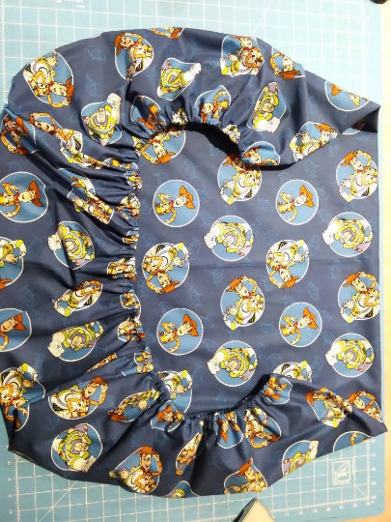 May include: Blue fabric with a repeating pattern of Toy Story characters in yellow, red, and white. The characters are in circles on a blue background. The fabric is gathered at the top and bottom.