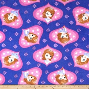 Peut inclure: Un tissu bleu avec un motif répété de cadres en forme de losange roses mettant en scène une princesse de dessin animé aux cheveux bruns et une couronne. La princesse porte une robe bleue et a un fond rose.