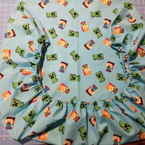 Peut inclure: Un drap-housse bleu clair avec un motif répété de personnages Minecraft verts et orange. Le drap est doté d'un élastique sur les bords.