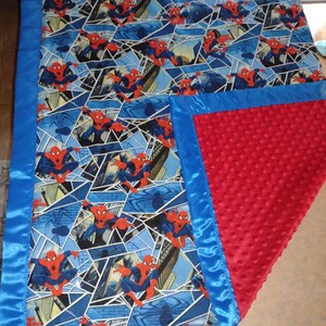 May include: A blue and red baby blanket with a Spiderman pattern on one side and a red minky fabric on the other side. The blanket has a blue satin trim.