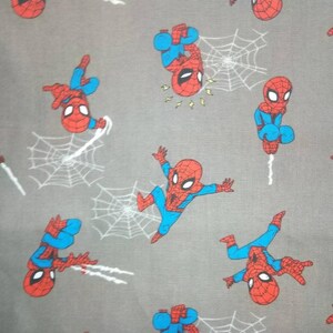 May include: A gray fabric with a repeating pattern of red and blue cartoon Spider-Man characters. The characters are in various poses, including swinging from a web, standing, and pointing.