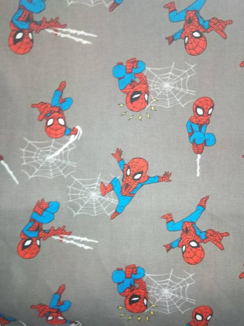 May include: A gray fabric with a repeating pattern of red and blue cartoon Spider-Man characters. The characters are in various poses, including swinging from a web, standing, and pointing.