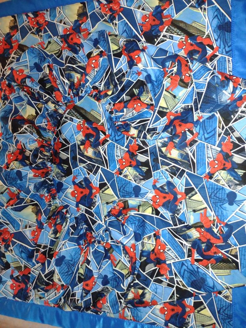 May include: A blue and red patterned fabric with a repeated image of Spiderman swinging through a city skyline.