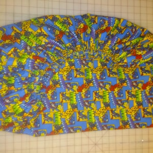 May include: A blue fabric with a repeating pattern of the word "BAM" in yellow, red, green, and purple. The fabric is folded in a fan shape.