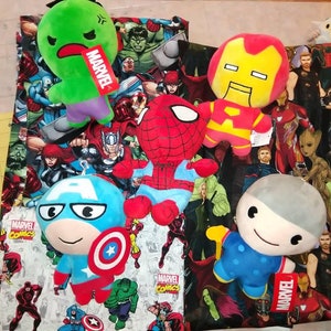 May include: A collection of plush toys featuring Marvel characters. The toys are arranged on a fabric background with a Marvel Comics print. The toys include Iron Man, Spider-Man, Captain America, Hulk, and a grey character with a blue shirt. The fabric background features a variety of Marvel characters, including Iron Man, Spider-Man, Captain America, Hulk, Thor, and Groot.