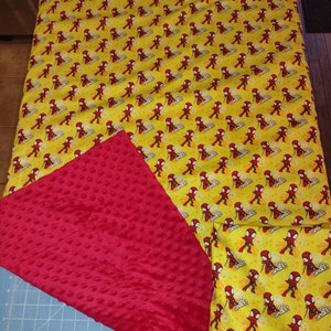 Puede incluir: Una manta reversible para bebé en rojo y amarillo con un patrón de Spiderman en un lado y una tela minky de puntos rojos en el otro. El lado de Spiderman presenta un patrón repetido de Spiderman con un traje rojo y azul con las palabras "Go Spider!" impresas en la tela.