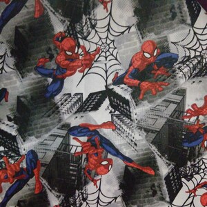 May include: A white fabric with a repeating pattern of Spiderman in a red and blue suit, swinging from a web in front of a gray and black cityscape.