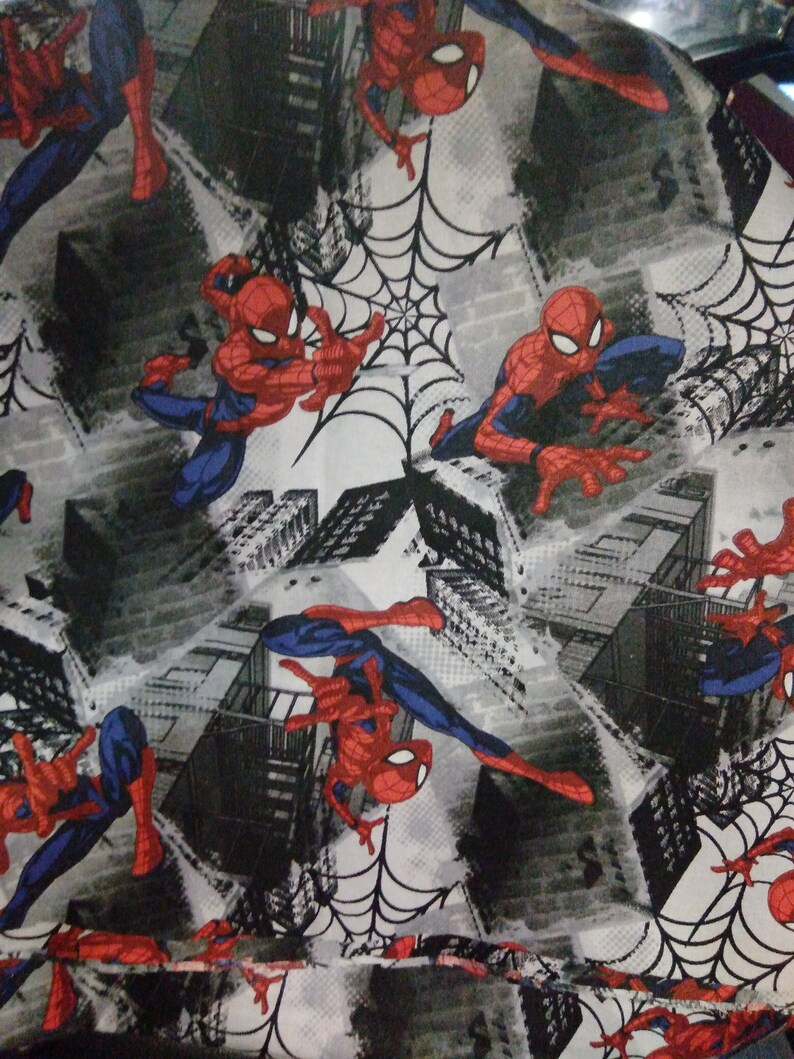 May include: A white fabric with a repeating pattern of Spiderman in a red and blue suit, swinging from a web in front of a gray and black cityscape.