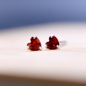 May include: A pair of heart-shaped earrings with red gemstones set in silver.