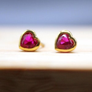 May include: A pair of gold heart-shaped earrings with red gemstones.