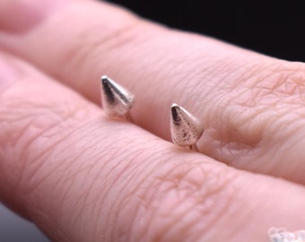 May include: A close-up of a hand wearing two silver spike earrings and a silver ring with a decorative design.