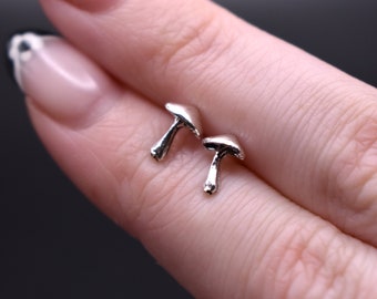 May include: A pair of silver mushroom stud earrings. The earrings are small and delicate, and they are perfect for adding a touch of whimsy to any outfit.