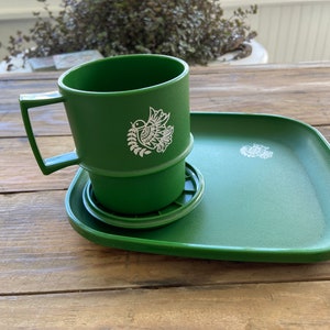 Könnte beinhalten: Eine grüne Plastiktasse mit einem weißen Vogelmotiv sitzt auf einem passenden grünen Plastiktablett. Die Tasse hat einen Griff und einen Deckel.