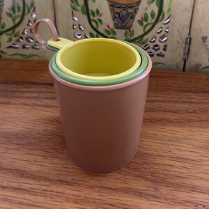 May include: A set of three nesting measuring cups in brown, green, and yellow. The cups are made of plastic and have a handle.