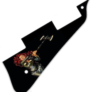 Pode incluir: Um pickguard de guitarra preto com uma borda branca. O pickguard apresenta uma ilustração colorida de uma mulher empunhando um machado.