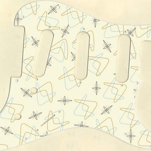 May include: A white guitar pickguard with a retro-style pattern of blue and gold lines and black stars. The pickguard has three cutouts for pickups.