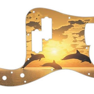 May include: A guitar pickguard with a sunset and dolphin silhouette design. The pickguard is a light brown color with a yellow sunset and three dolphins jumping in the water.