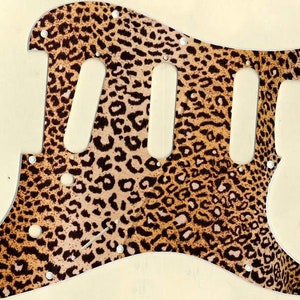 May include: A brown and black leopard print guitar pickguard with three cutouts for pickups.