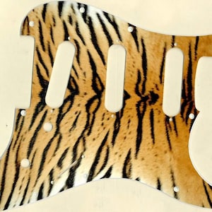 May include: A tiger print guitar pickguard with three pickup cutouts and multiple screw holes.